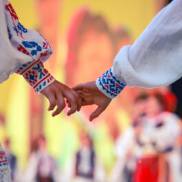 Un băiat și o fată îmbrăcați în costume populare se țin de mână