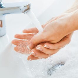 Două mâini, cu manichiura french, poziționate sub jet de apă, într-o chiuvetă