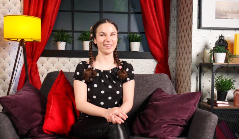 Andrada Precup, pe canapeaua unui studio de filmări, suprinsă în timp ce zâmbește în cadrul unui interviu