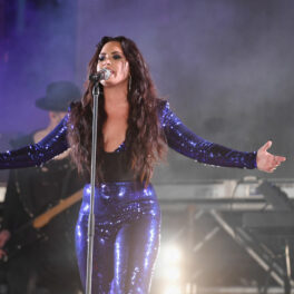 Demi Lovato pe scenă îmbrăcată cu o salopetă mulată strălucitoare și albastră cu decolteu adânc