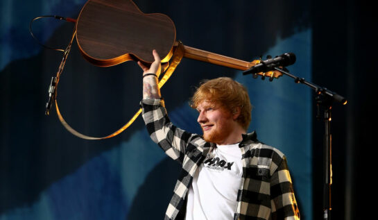 Ed Sheeran, fotografiat în timp ce își ridică chitara pentru a saluta fanii în timpul unui concert