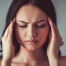 O femeie stresată, cu părul desfăcut, își atinge tâmplele