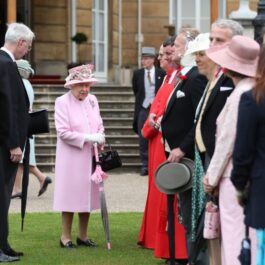 Regina în grădina Palatului Buckingham înconjurată de înalți oficiali