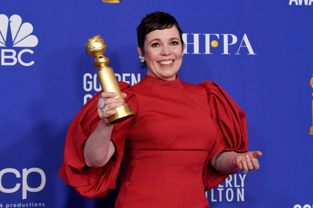 Olivia Colman îmbrăcată cu o rochie roșie pe covorul roșu ține în mână un Glob de Aur
