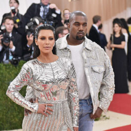 Kanye West îmbrăcat cu o jachetă argintie cu aplicații stă în spatele lui Kima Kardashian îmbrăcată cu o rochie argintie pe covorul roșu la Met Gala
