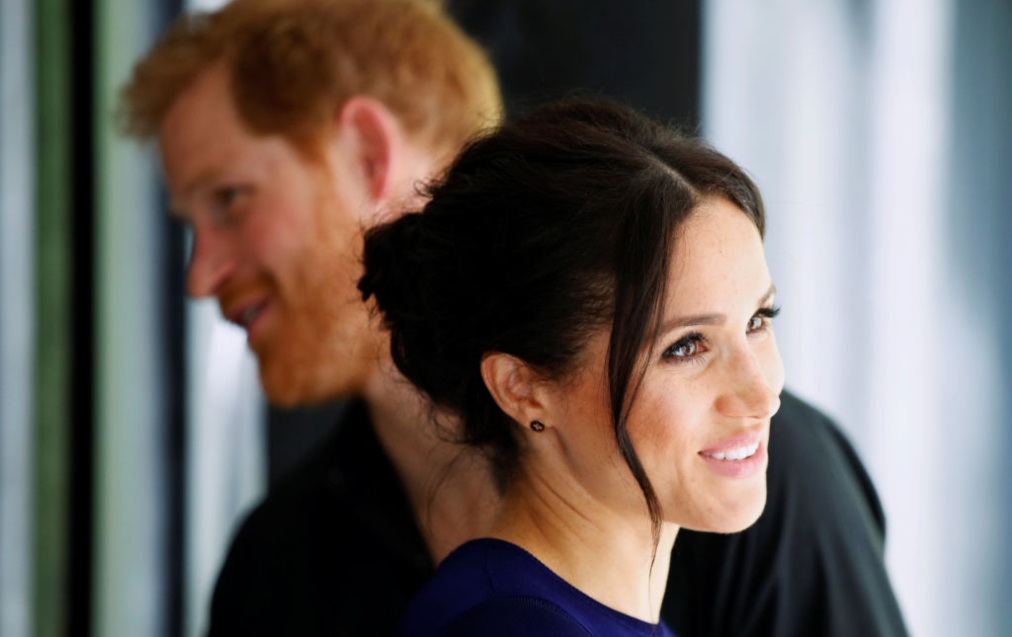 Portret cu Meghan Markle și Prințul Harry în spatele ei