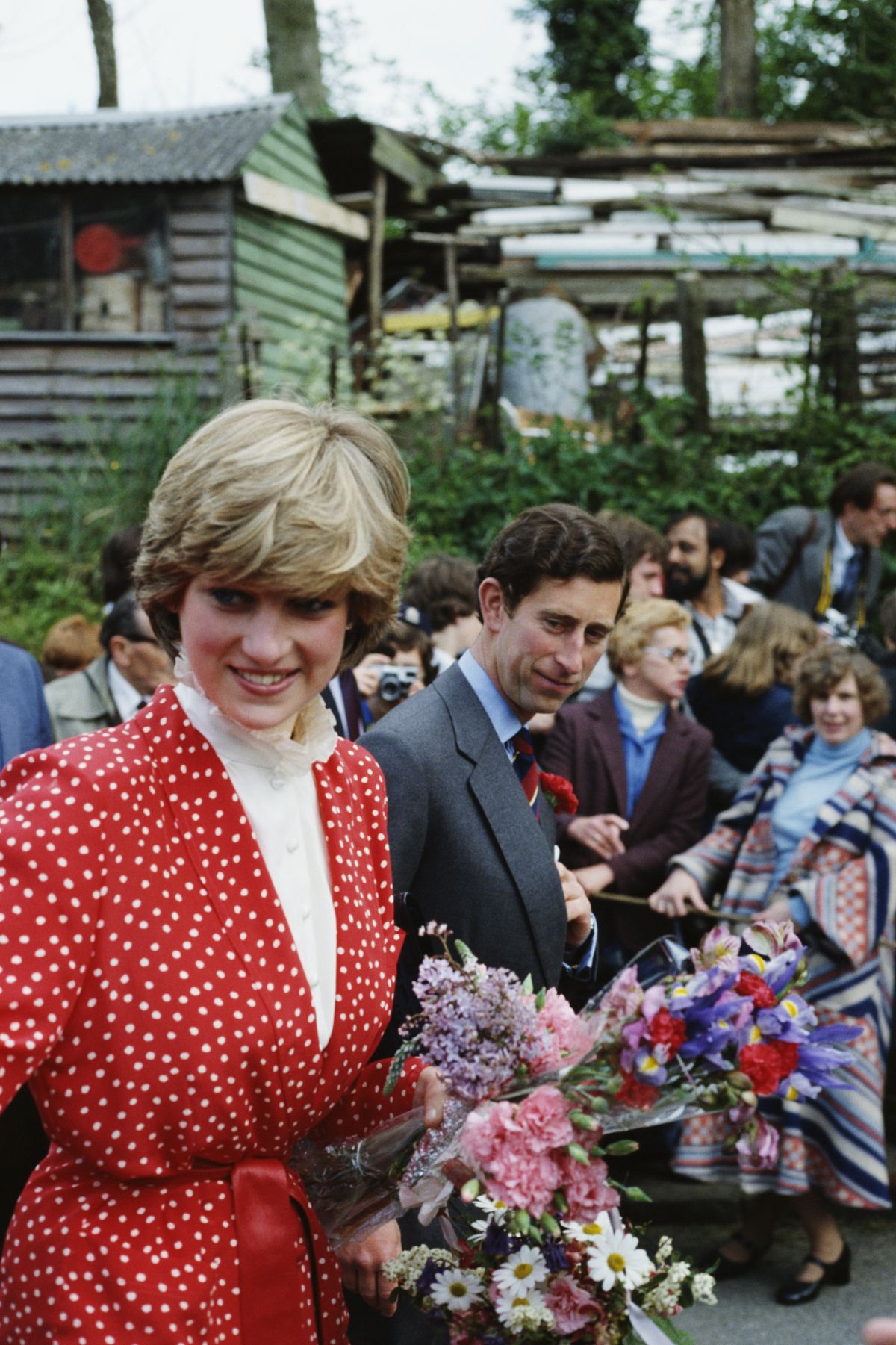 Lady Diana, alături de Prințul Charles, poartă o rochie roșie, cu buline și guler încrețit, și ține în mână un buchet de flori.