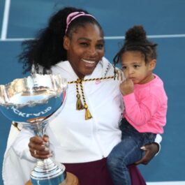 Serena Williams își ține fiica ăn brațe și trofeul în mână pe terenul de tenis