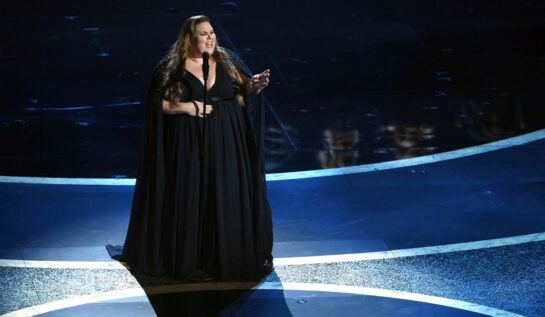 Chrissy Metz, îmbrăcată într-o rochie neagră, de gală, vorbește în fața unui microfon