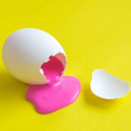 Un ou alb, spart, din care curge vopsea roz, pe un fundal galben
