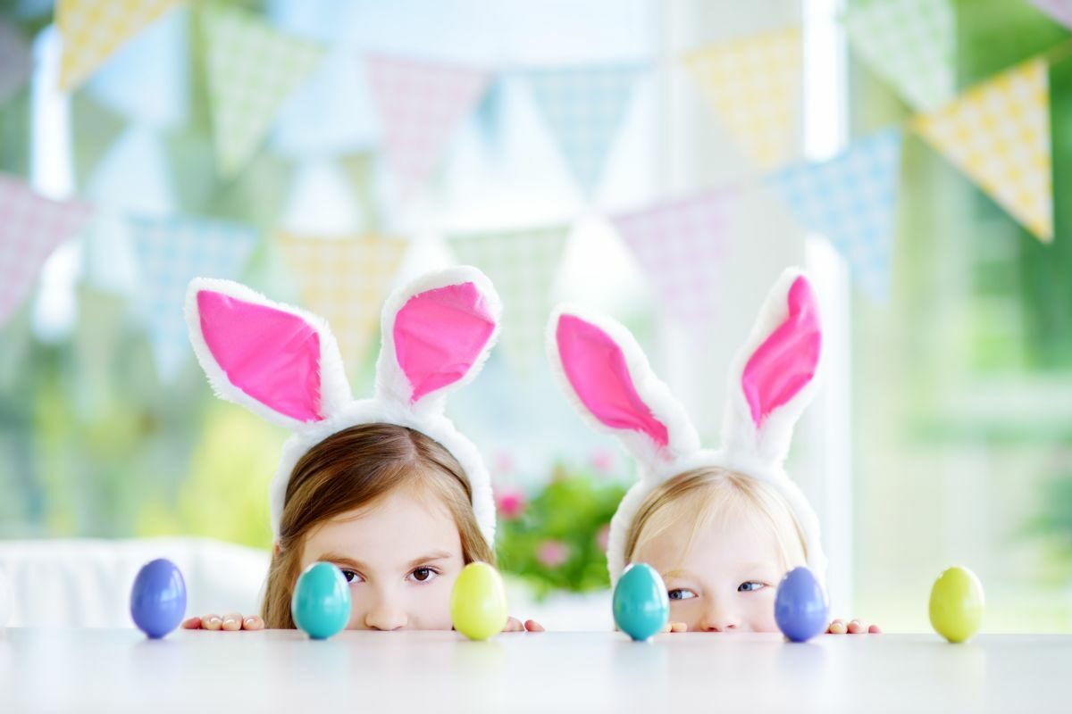 Două fetițe, ce poartă urechi de iepurași, se joacă cu ouă colorate