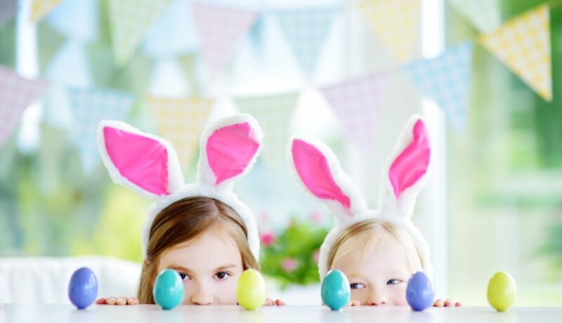 Două fetițe, ce poartă urechi de iepurași, se joacă cu ouă colorate