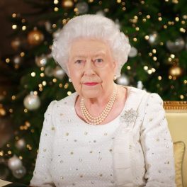 regina elisabeta îmbrăcată într-o ținută albă cu o diademă pe cap în fașa unui brad de Crăciun în timp ce poartă brășa sub formă de stea