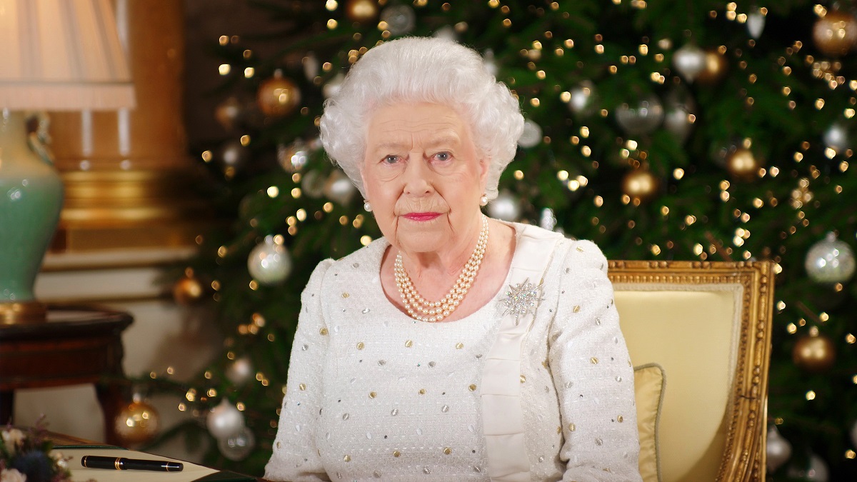 regina elisabeta îmbrăcată într-o ținută albă cu o diademă pe cap în fașa unui brad de Crăciun în timp ce poartă brășa sub formă de stea