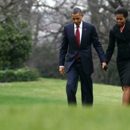 Michelle și Barach Obama, ținându-se de mână, pe o pajiște verde