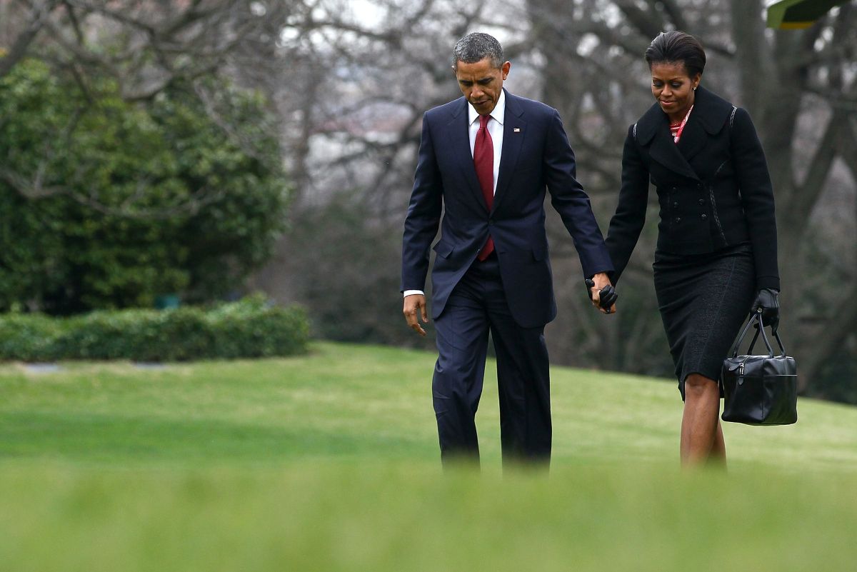 Michelle și Barach Obama, ținându-se de mână, pe o pajiște verde
