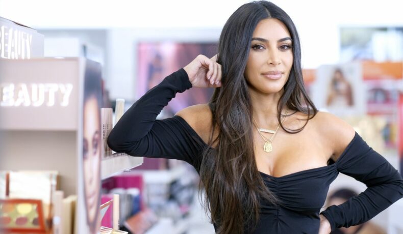 Kim Kardashian, cu o ținută de miliardară, purtând un top de culoare neagră, langă un raft de cosmetice