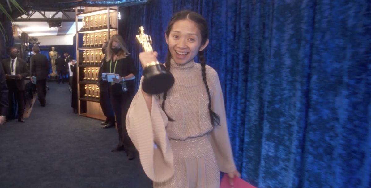 Chloe Zhao, într-o ținută elegantă, cu două cozi împletite, ține în mână un trofeu Oscar, la ceremoonia de decernare a premiilor din anul 2021.