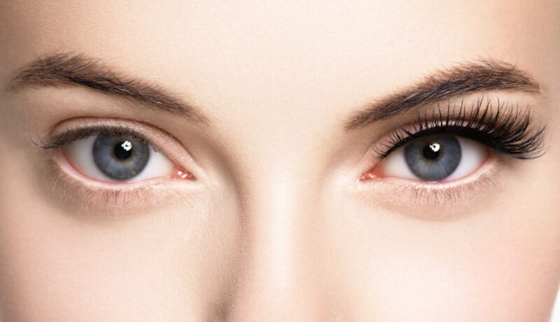 O femeie cu gene false la ochiul drept, cum privești spre poză. La ochiul stâng are genele naturale. În poză se poate observa diferența înainte și după aplicarea genelor false.