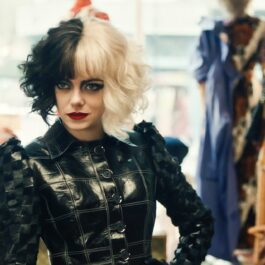 Emma Stone apare în lista de filme noi în Cruella îmbrăcată cu o bluză neagră de piele cu părul vopsit jumătate alb și jumătate negru