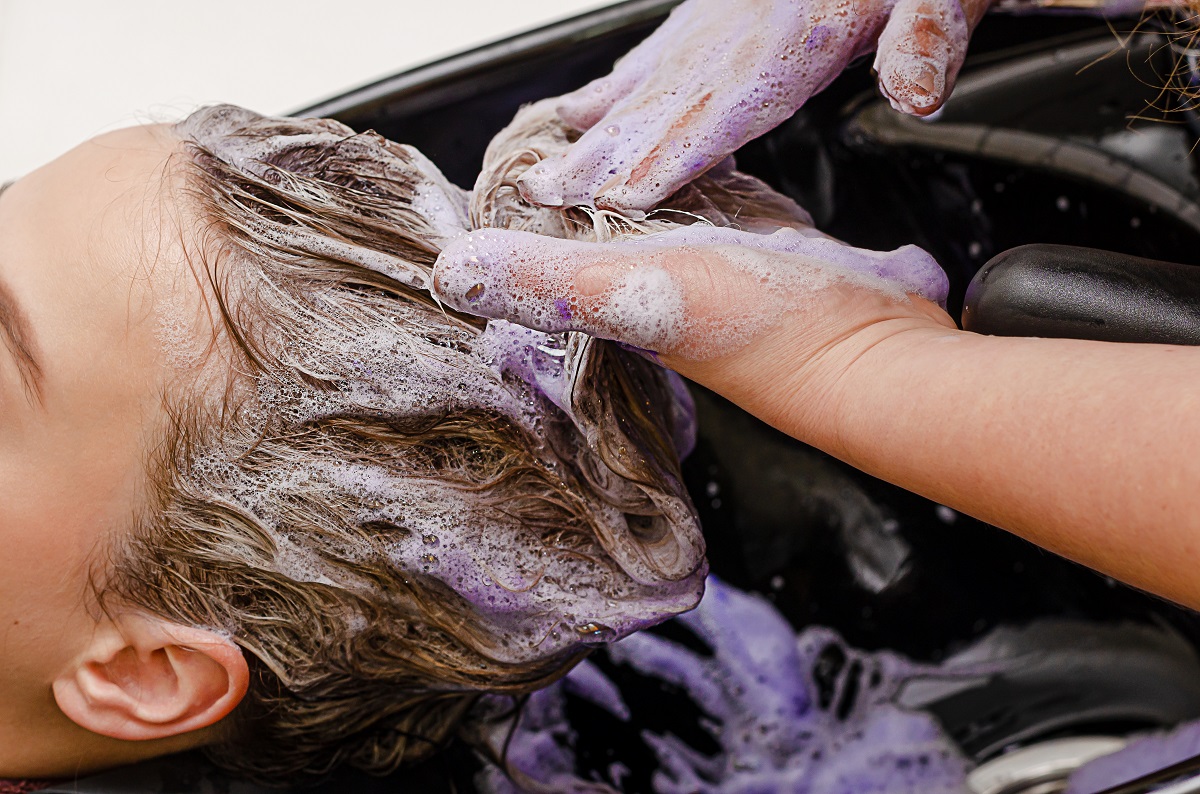 femeie care se spală pe păr cu șampon mov pentru a demonstra efectele acestuia
