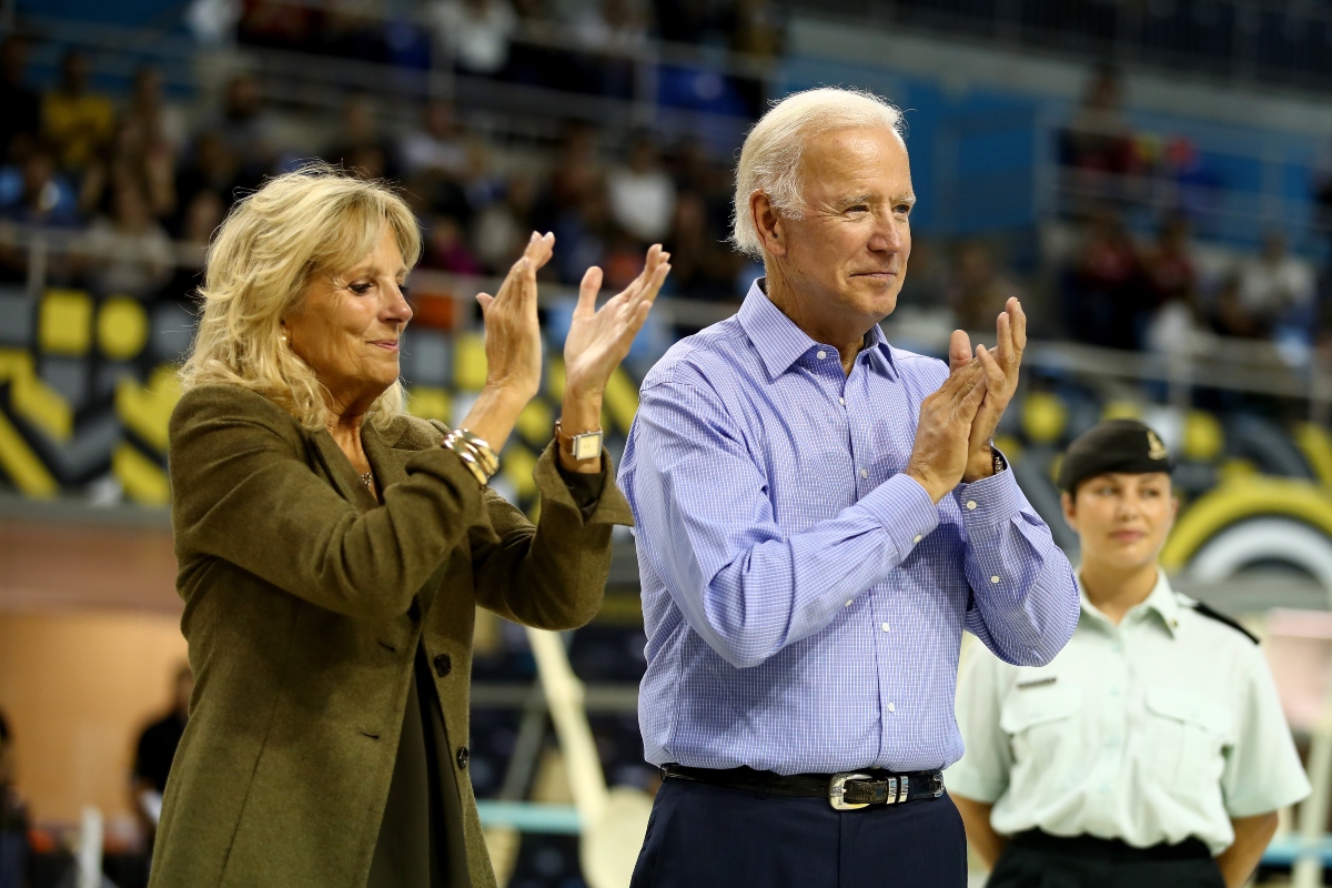 Jill Biden alături de Joe Biden. Amândoi aplaudă. Ea are părul pe spate și poartă o haină de culoare kaki. El are o cămașă albastru deschisși niște pantaloni negri.