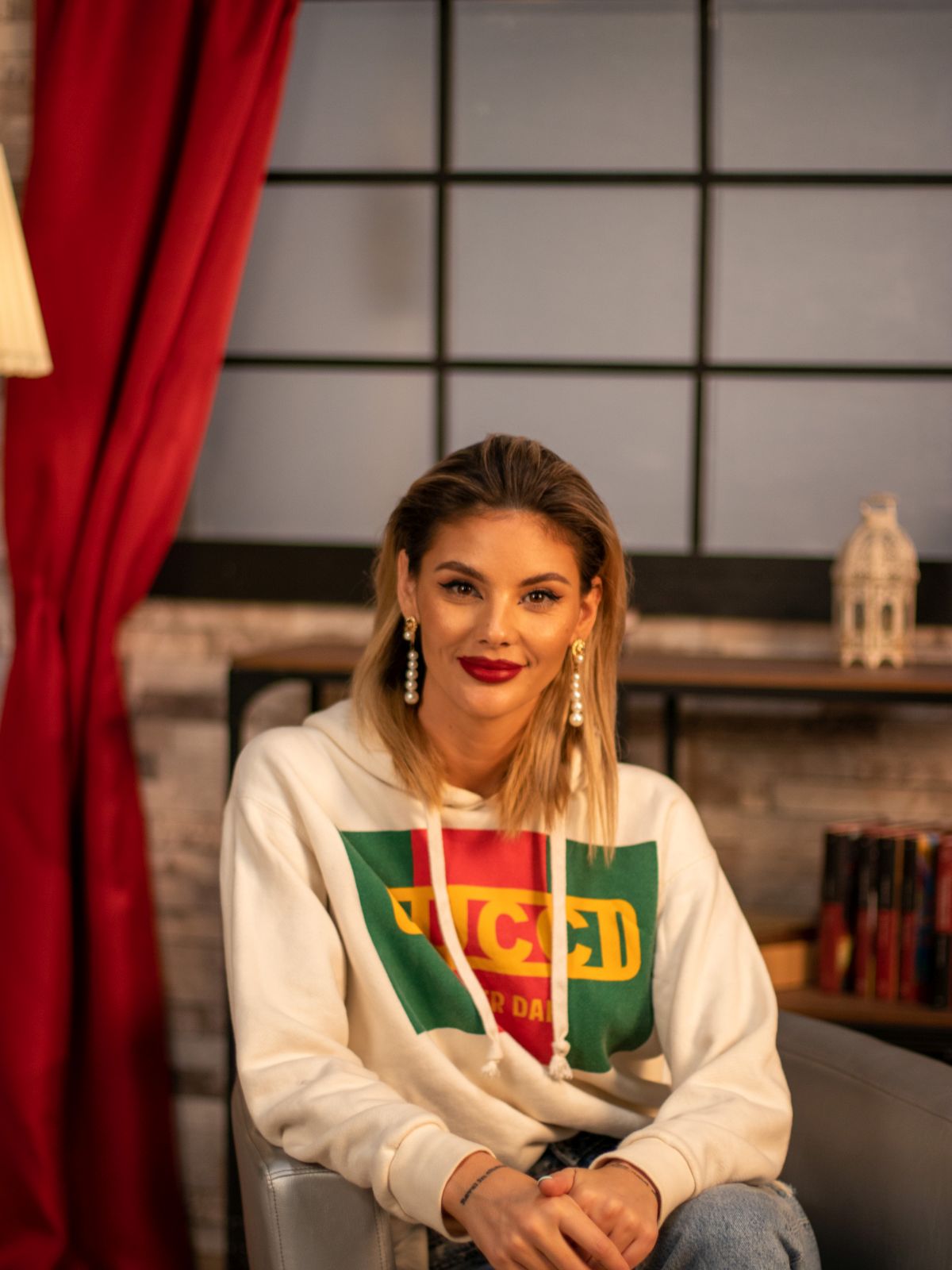 Ramona Olaru, îmbrăcată cu un hanorac Gucci și o pereche de blugi deschiși la culoare, stă pe un scaun în studioul CaTine.ro.