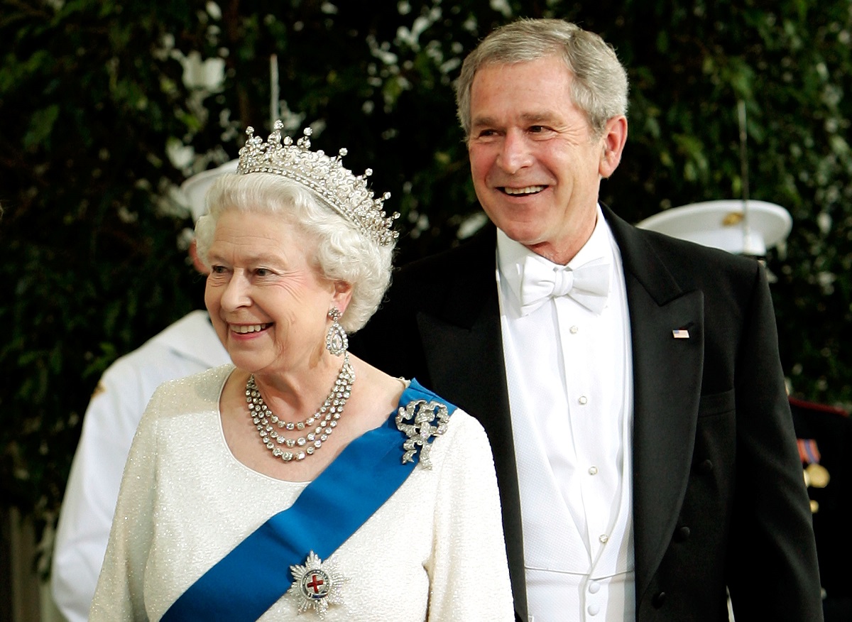 regina elisabeta într-un costum alb purtând o diademă și broșa reginei Maria alături de președintele Bush îmbrăcat într-un costum negru