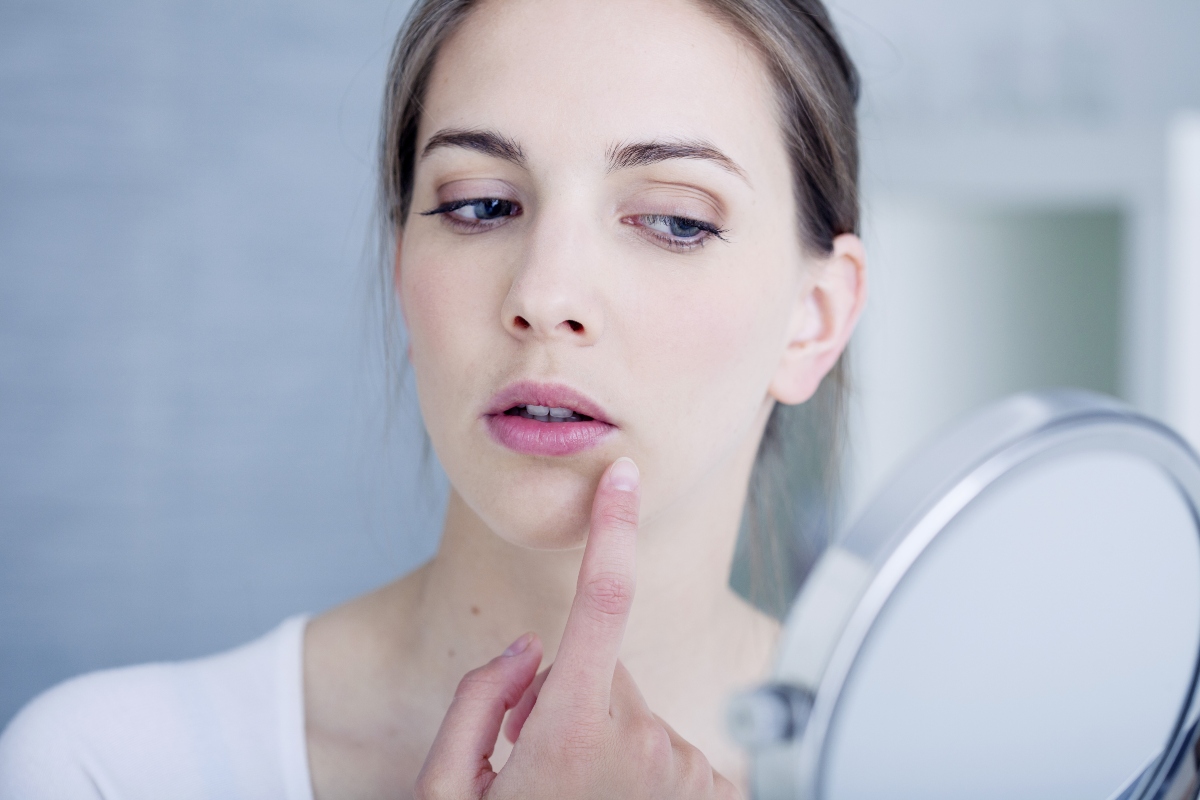 O femeie cu buze crăpate are părul strâns la spate, se privește într-o oglindă rotundă