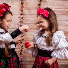 Două fetițe, îmbrăcate în costum tradițional, în timp ce ciocnesc ouă roșii