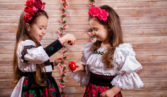 Două fetițe, îmbrăcate în costum tradițional, în timp ce ciocnesc ouă roșii