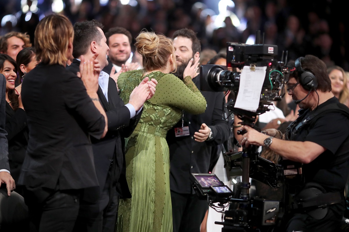 Adele la gala Premiilor Grammy îmbrăcată într-o rochie verde lungă în timp ce își sărută soțul și este aplaudată de public