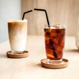 două pahare cu pai negru așezate pe un blat de lemn care ilustrează Cold Brew vs Iced Coffee și felul cum se prepară și care este diferența dintre ele