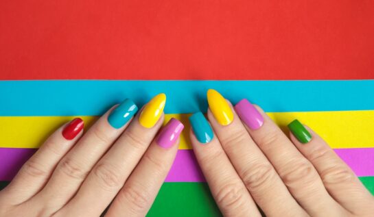 două mâini pe un fundal colorat cu unghiile făcute în nuanțe de roșu, albastru, galben, violet și verde care ilustrează cum să îți alegi forma ideală pentru unghii