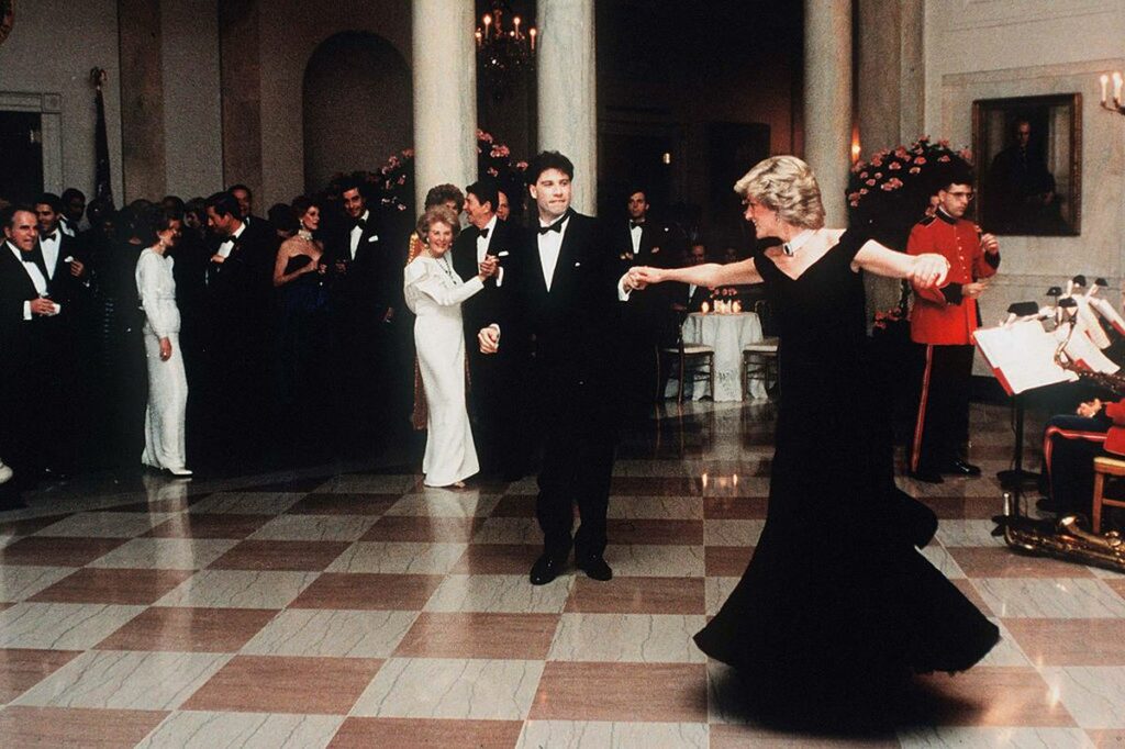 John Travolta, îmbrăcat în costum negru, dansează cu Prințesa Diana, ce poartă o rochie de gală, de culoare neagră