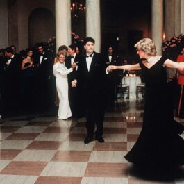 John Travolta, îmbrăcat în costum negru, dansează cu Prințesa Diana, ce poartă o rochie de gală, de culoare neagră