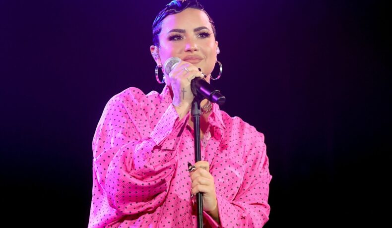 Demi Lovato pe scenă în fața microfonului îmbrăcată într-o rochie roz la premiera evenimentului documentarului său Dancing with the devil în martie 2021