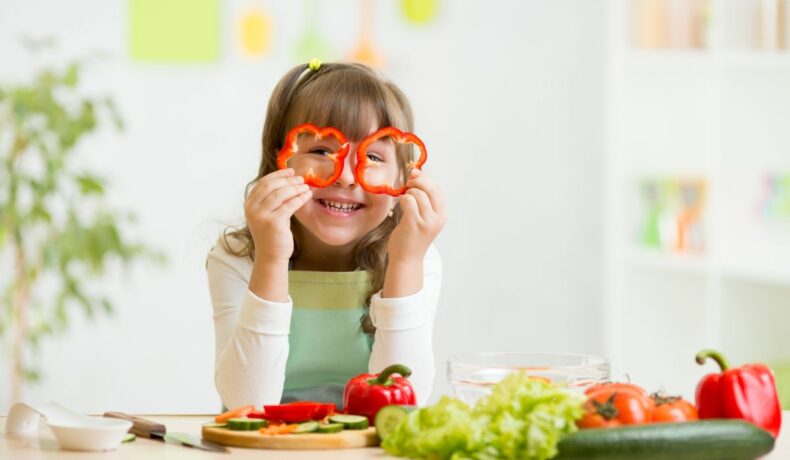 O fetiță care zâmbește, își pune două rondele de ardei pe post de ochelari