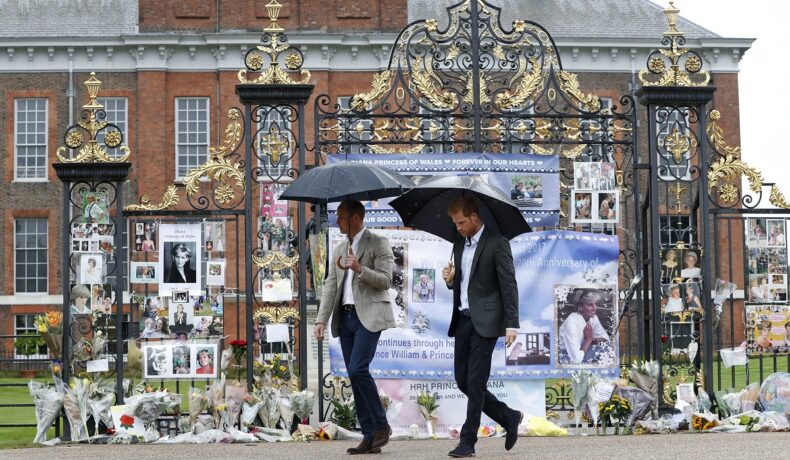 Prințul William alături de Prințul Harry în timp ce țin două umbrele și trec prin fața porții Castelului Kensington în 2017 înainte să afle adevărul despre interviul Prințesei Diana