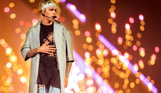 Justin Bieber s-a lăsat pe mâinile stiliștilor și este îmbrăcat într-un tricou negru și o cămașă gri desfăcută, cu părul prins într-o bandană albă în timp ce în spatele său apare publicul plin de lumini