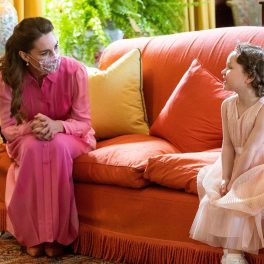 Kate Middleton într-o rochie lungă roz stând pe o canapea orange alături de micuța Mila Sneddon îmbrăcată la fel ca o prințesă