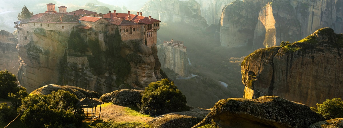 fotografie care surprinde orașul Meteora din Grecia cu stâncile acoperite de verdeață și casele localnicilor situate în vârf de creste