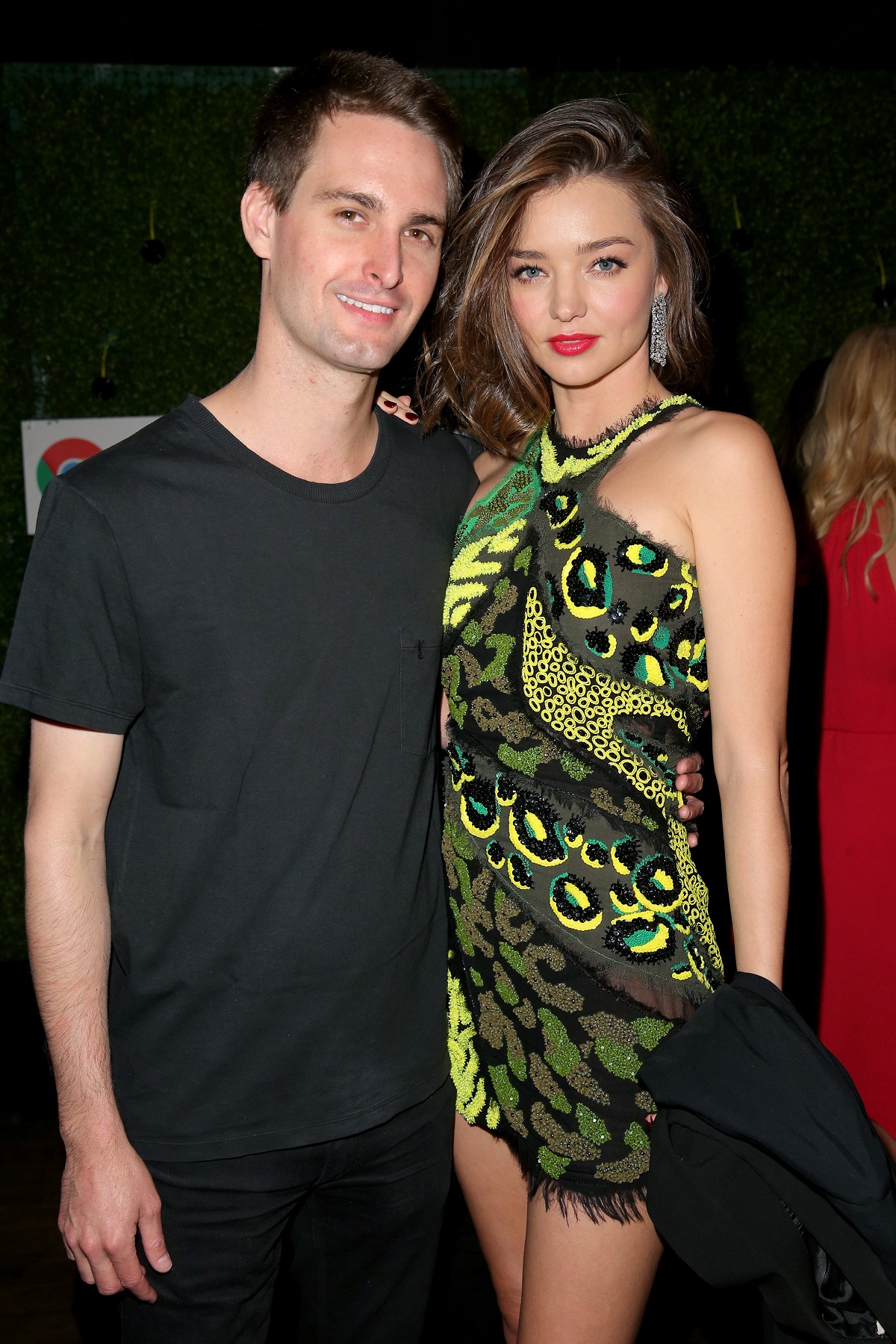 Miranda Kerr îmbrăcată într-o rochie verde cu paiete alături de soțul ei Evan Spiege la un eveniment public numit Republic Records Grammy în timp ce zâmbesc la cameră