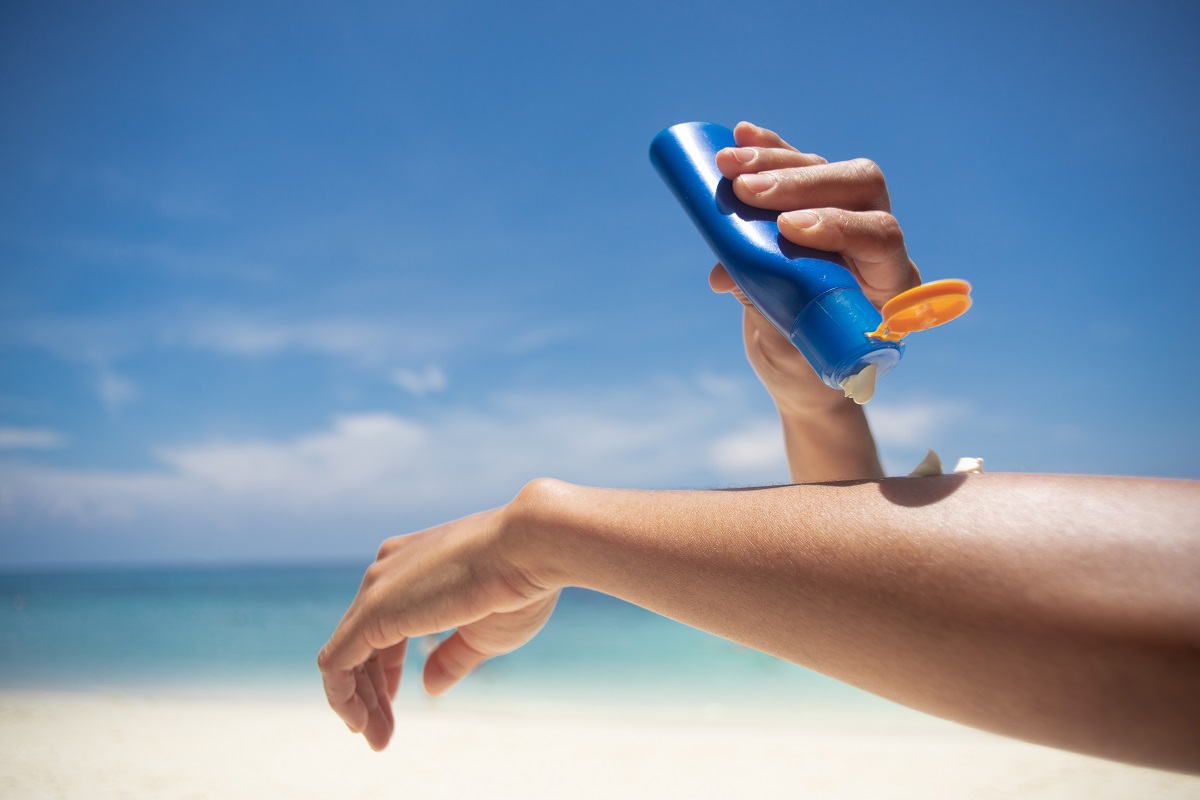 O femeie care își aplică pe brațe produse cu protecție solară în timp ce se află pe o plajă