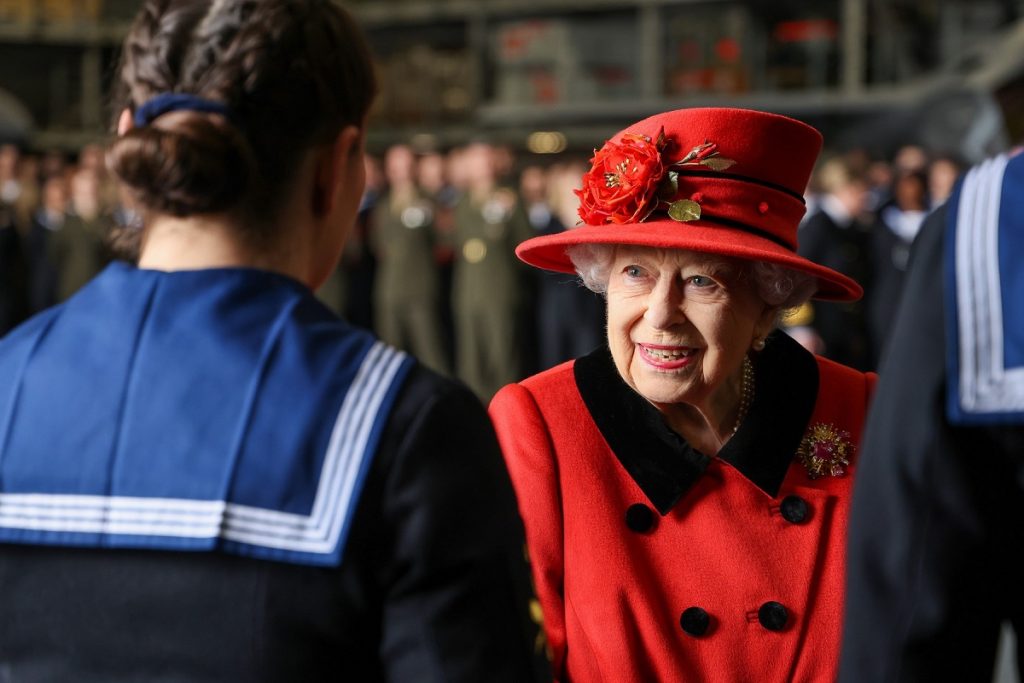 Regina Elisabeta purtând o pălărie roșie și un palton roșu, la care a asortat o broșă pentru a aduce un omagiu PrințuluiPhilip la vizita sa oficială a portavionului HMS Regina Elisabeta