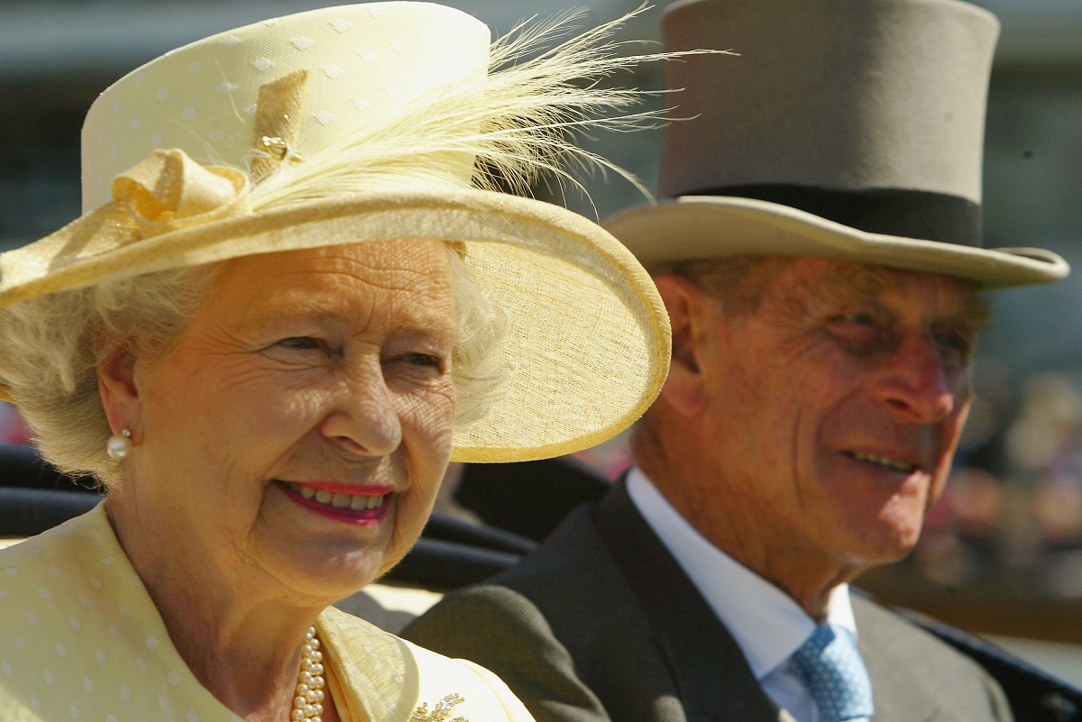 Portret cu Regina Elisabeta purtând o bluză și o pălărie cu pană galbene, alături de amintirea Prințului Philip îmbrăcat la costum și purtând o pălărie înaltă gri
