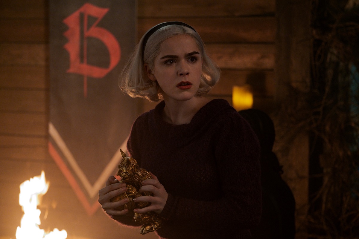 Personajul principal Sabrina în timp ce ține în mână o statuetă de aur și este îmbrăcată într-un hanorac negru