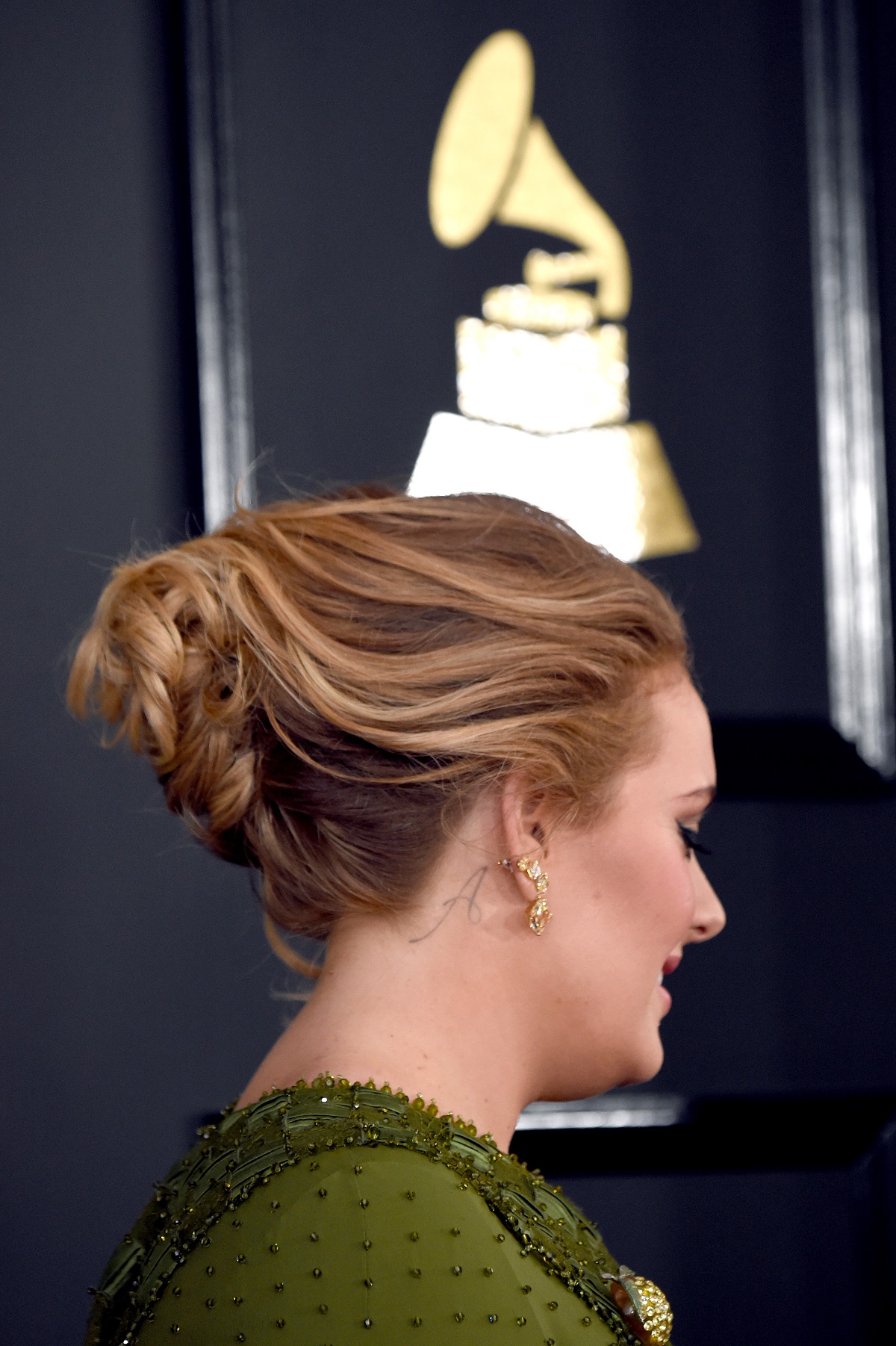 Portret cu Adele din profil având părul prins într-un coc, unde se poate observa tatuajul cu litera A după ureche