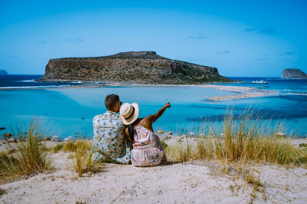 Un cuplu ce stă pe plajă și amiră peisajul, în Creta, Grecia