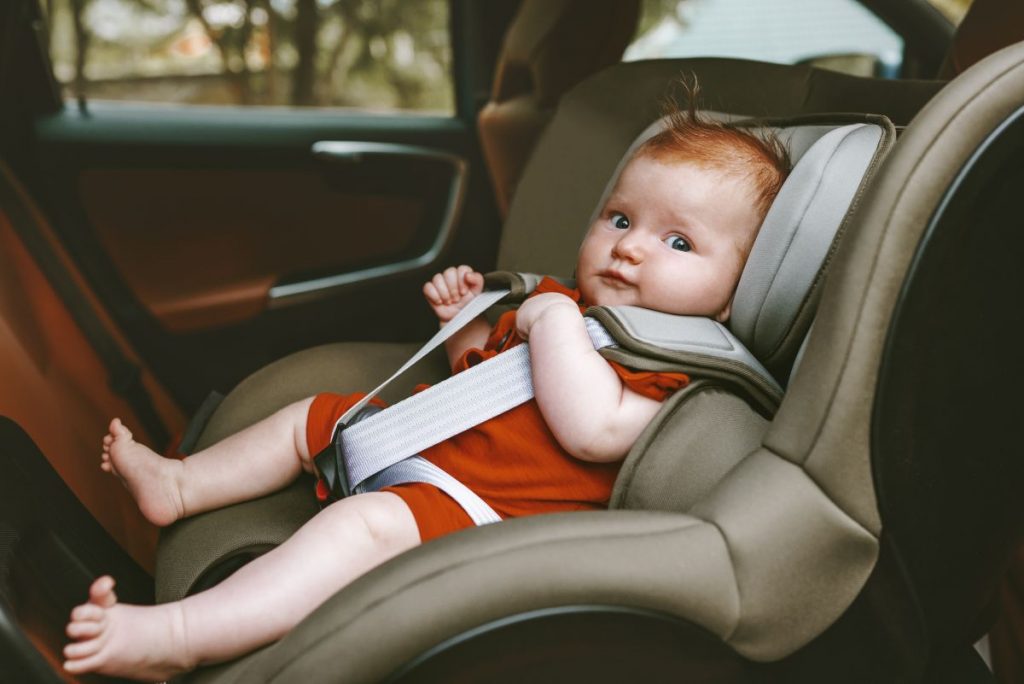 Un bebelul, îmbrăcat în arămiu, este așezat într-un scaun rear-facing